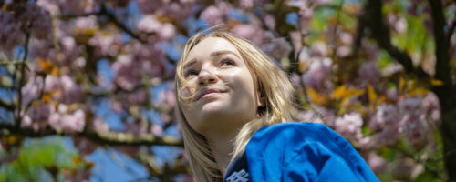 kvindelig elev står under lyserøde kirsebærtræer