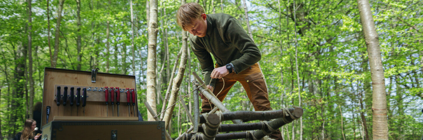 Elev står og arbejder med knive i naturen