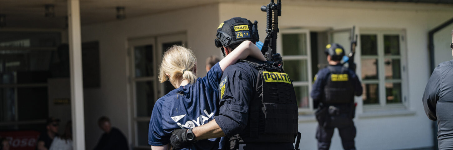 Mand i politiuniform hjælper en kvindelig øvedeltager med at gå