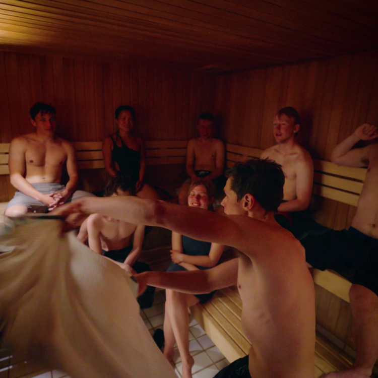 Gusmester vifter et klæde i sauna fyldt med højskoleelever